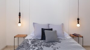 En snyggt bäddad säng med ett blommigt överkast, två sängbord med böcker och två hänglampor med synliga glödlampor.