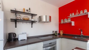 Ett modernt kök med vita skåp, en rostfri köksfläkt, en kaffebryggare, en brödrost och en röd accentvägg.