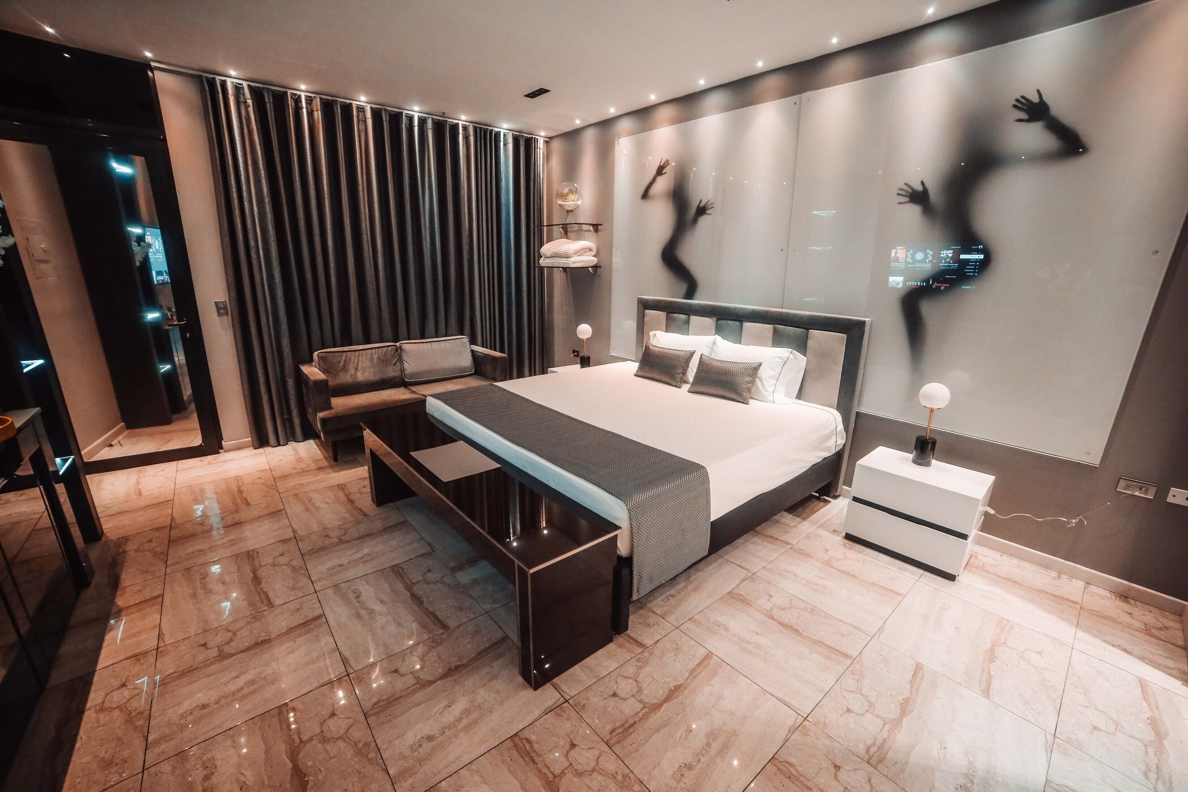 Un dormitorio moderno con una cama grande, mesitas de noche, un banco y un televisor montado en la pared.