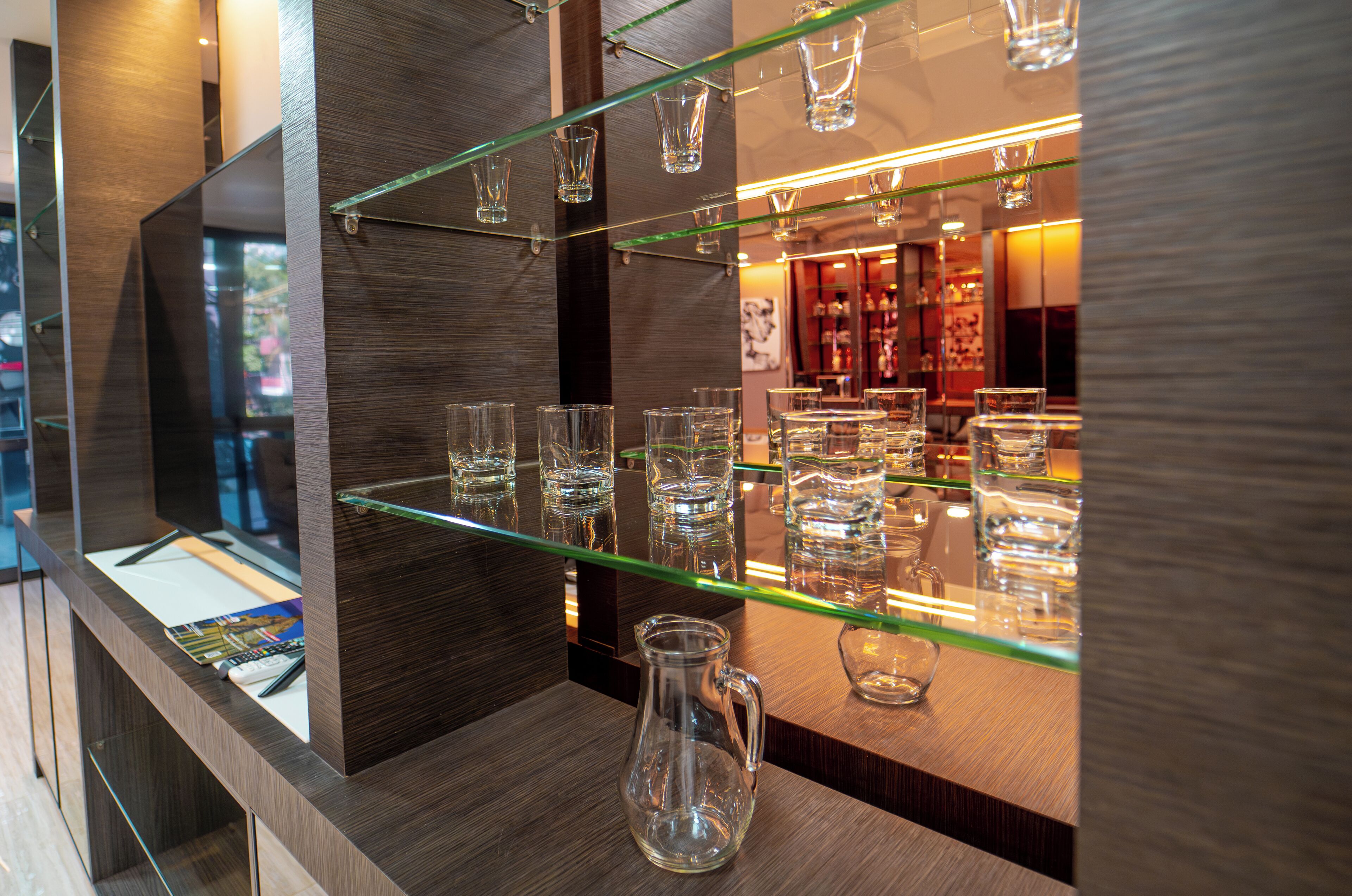 Un espace bar avec des étagères en verre où sont exposés différents types de verres et une carafe.