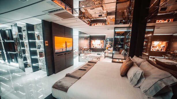 Una habitación de hotel moderna con una cama grande, televisión, chimenea y un separador de vidrio con estantes.