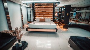 Una habitación de hotel moderna con una cama grande, un área de descanso con sofá y mesa de centro, y un jarrón decorativo con flores.
