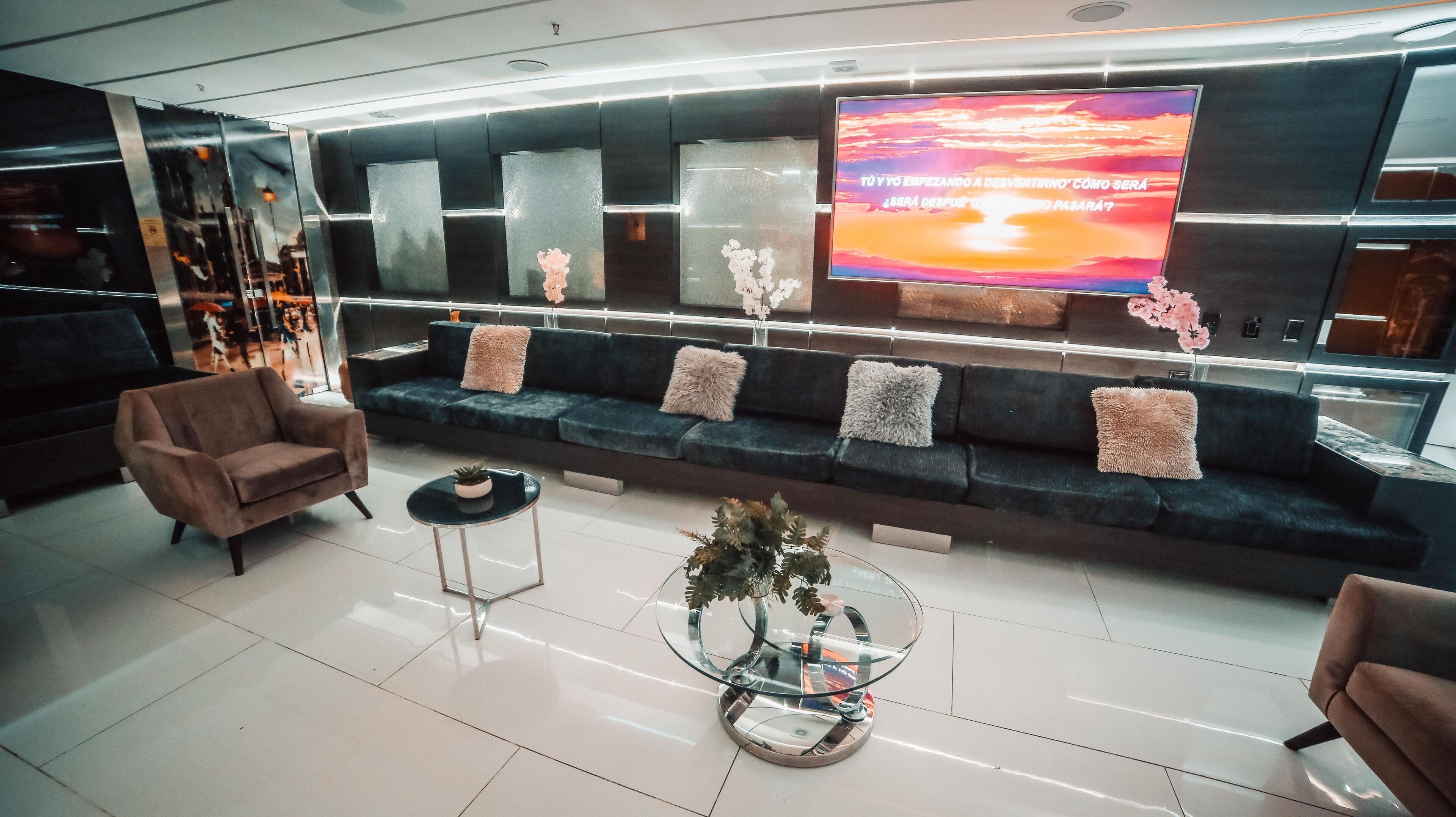 A modern lounge area with a sofa, armchairs, a glass coffee table, and a TV screen displaying text.