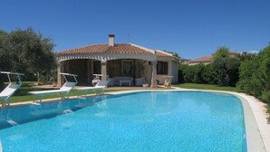 A swimming pool with lounge chairs, a covered patio, and a house with a tiled roof. - Rei Sole (REI308) by Interhome (Costa Rei)