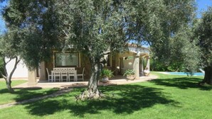 A building with a covered patio area, a lawn, and a tree in the foreground. - Rei Sole (REI308) by Interhome (Costa Rei)