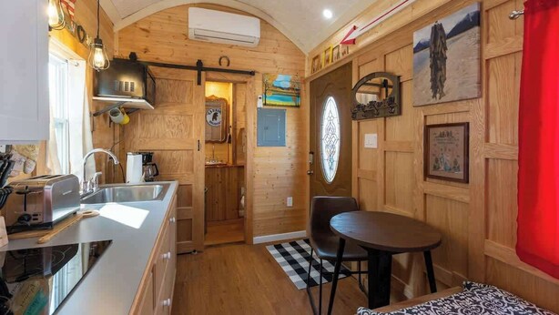 A compact kitchen with a sink, toaster, and wooden cabinets. A dining area with a table and chairs is visible. - Tiny House Martin - Pet Friendly (Leadville)
