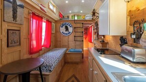 A compact, well-lit kitchen with wooden cabinetry, a built-in bench, and a dining table. - Tiny House Martin - Pet Friendly (Leadville)
