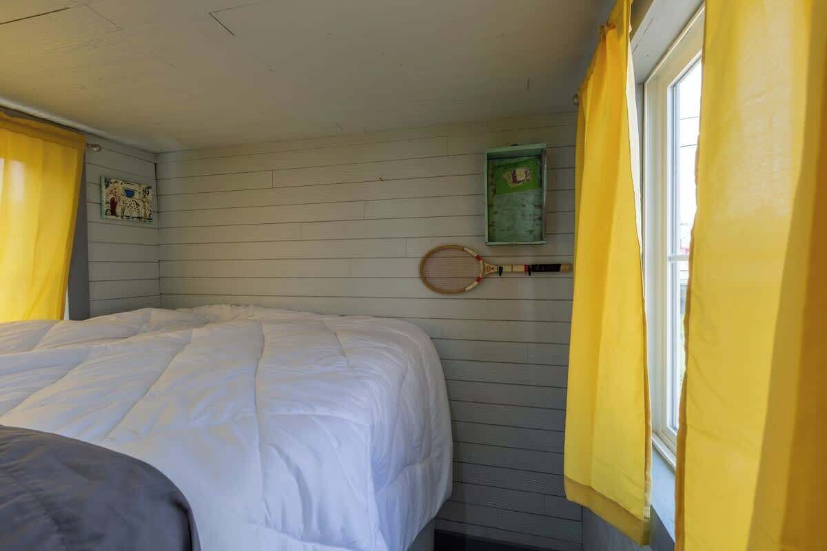 A room with a bed, a window with yellow curtains, and a tennis racket hanging on the wall.