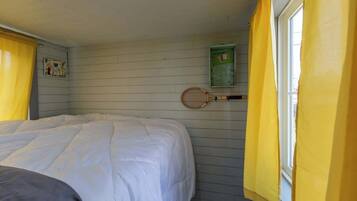 A room with a bed, a window with yellow curtains, and a tennis racket hanging on the wall.
