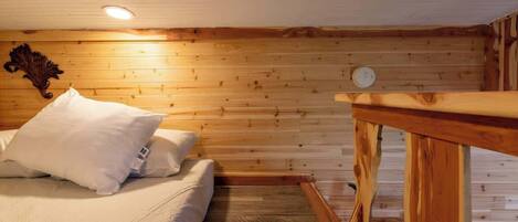 Una habitación con paneles de madera, una cama, una mesa de madera y una lámpara fijada a la pared.