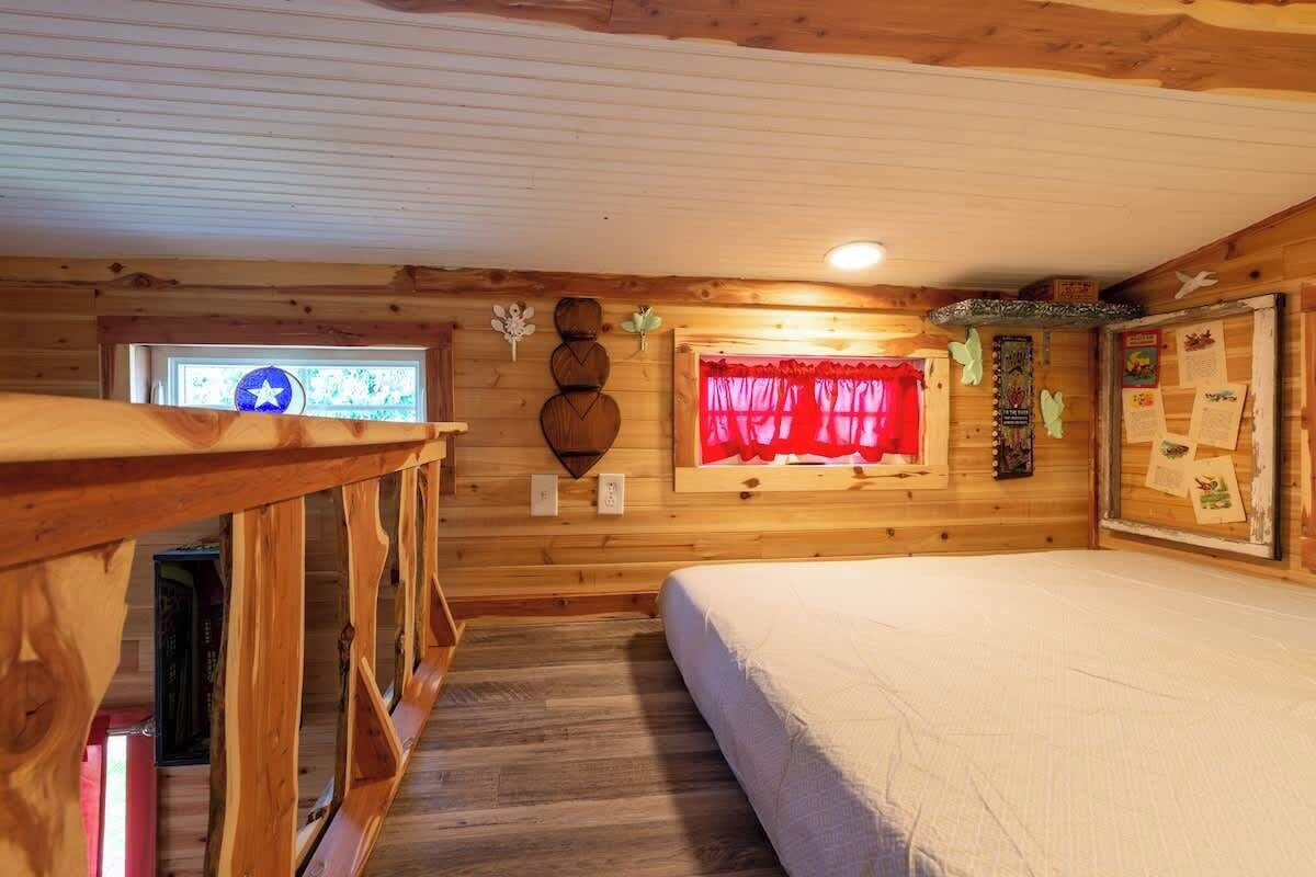 A cozy wooden cabin room with a bed, a small desk, and a window with a star decoration.