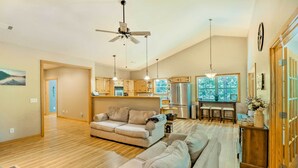 A spacious living room with a large sofa, a dining area with a kitchen in the background, and a ceiling fan. - Heber Springs Family Lake House: Fire Pit & Decks (Heber Springs)