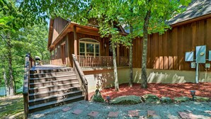 A wooden cabin with a porch and steps leading to a deck, surrounded by trees and rocks. - Heber Springs Family Lake House: Fire Pit & Decks (Heber Springs)