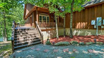 Une cabane en bois dotée d’un porche et d’un escalier menant à une terrasse, entourée d’arbres et de rochers.