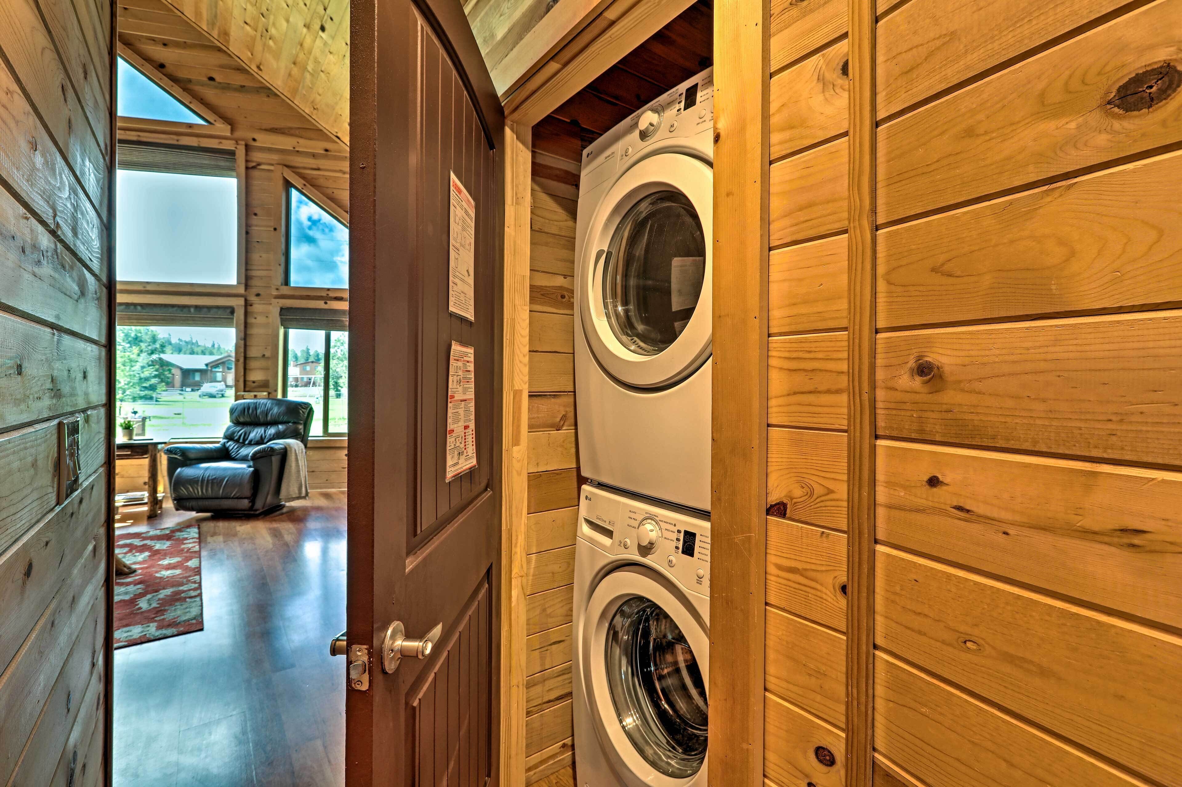 A laundry room with a front-loading washer and dryer, wooden walls, and a view of a covered outdoor area with a chair and rug.
