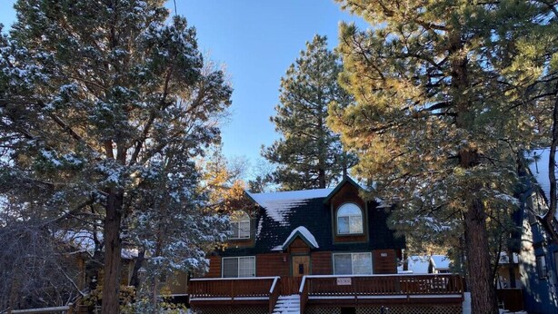 Une cabane dotée d’un toit à forte pente, entourée d’un paysage enneigé et de grands arbres à feuilles persistantes.