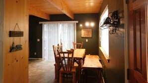 Un coin repas en bois avec une table et des chaises, une fenêtre avec des rideaux et un luminaire fixé au mur.