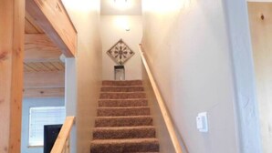 Un escalier recouvert de moquette, avec des rampes en bois, un élément décoratif au sommet et un interrupteur sur le mur.