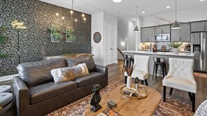 Una sala de estar moderna con un sofá de cuero oscuro, una mesa de centro con objetos decorativos y una pared estampada.