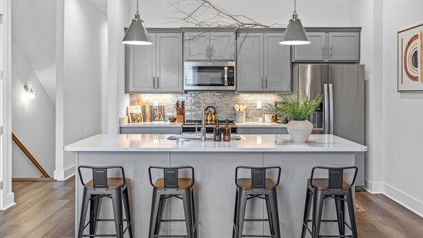 Una cocina moderna con armarios grises, electrodomésticos de acero inoxidable y una isla central con taburetes de bar.