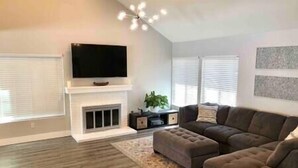 Een woonkamer met een open haard, een grote flatscreen-tv, een hoekbank en een decoratief vloerkleed.