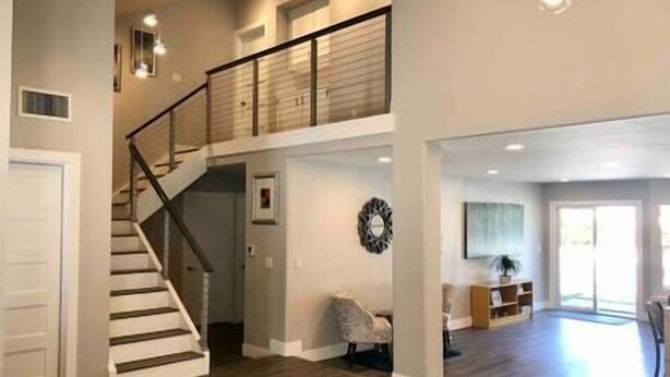 Een ruime woonkamer met een trap naar een hoger gelegen verdieping, een groot raam dat voor natuurlijk licht zorgt en een decoratief wandobject.