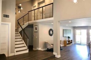 Uma ampla sala de estar com escada para um andar superior, uma janela grande que proporciona luz natural e um objeto decorativo na parede.