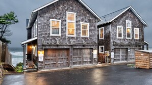 A two-story wooden house with a garage, located near the ocean. - Expansive Ocean Views From Home and Hot Tub, Pet Friendly, Private Deck, Fireplace, Steps From Beach (Depoe Bay)