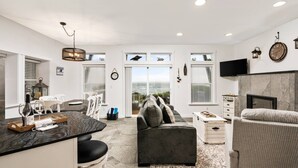 A modern living room with a dark grey sofa, a white armchair, and a patterned rug. - Expansive Ocean Views From Home and Hot Tub, Pet Friendly, Private Deck, Fireplace, Steps From Beach (Depoe Bay)