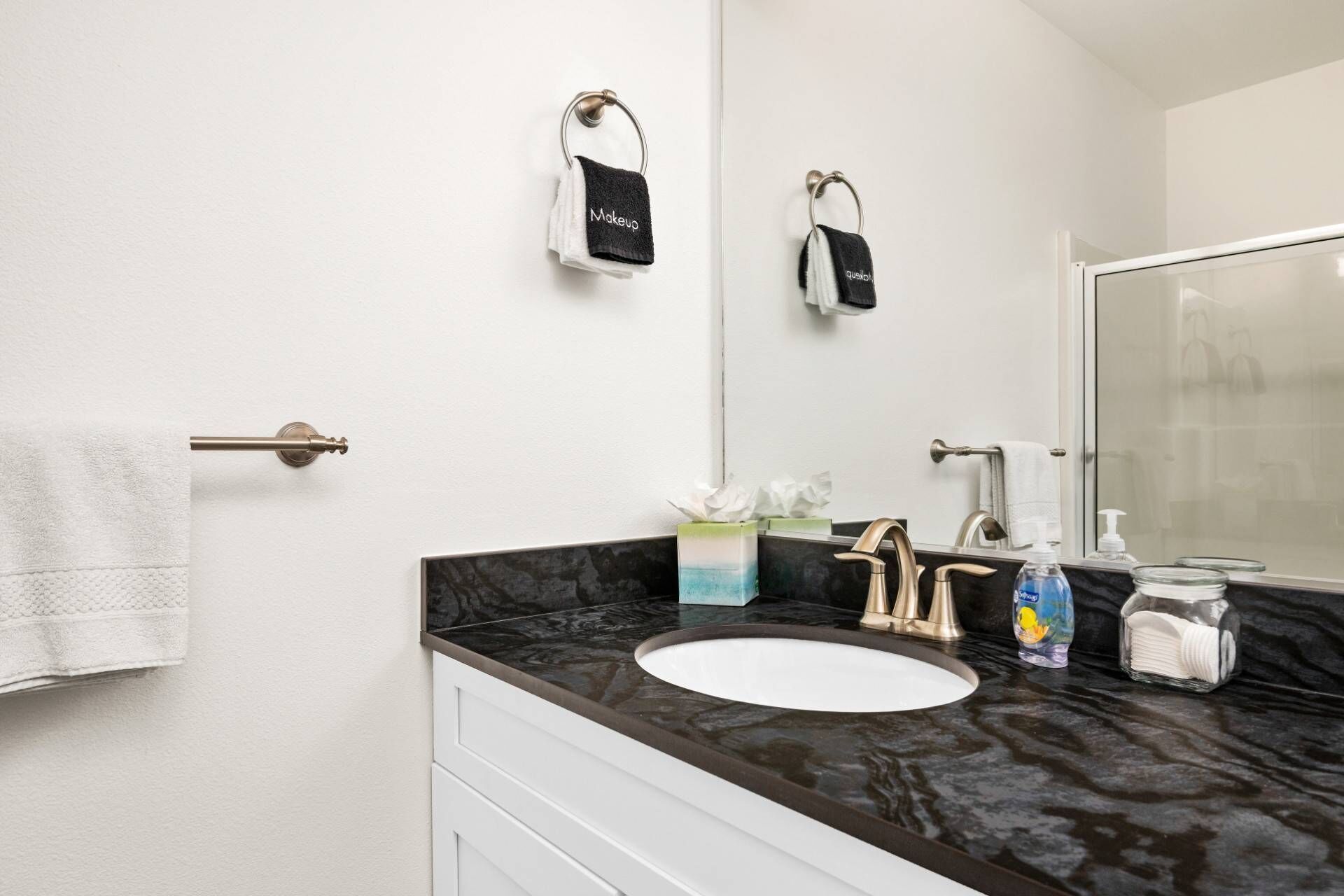 A bathroom with a white sink, a mirror, a towel rack, and a soap dispenser.