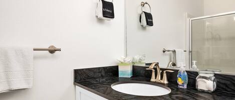 A bathroom with a white sink, a mirror, a towel rack, and a soap dispenser.