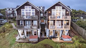 A two-story wooden house with balconies, a staircase, and a deck with outdoor furniture. - Expansive Ocean Views From Home and Hot Tub, Pet Friendly, Private Deck, Fireplace, Steps From Beach (Depoe Bay)