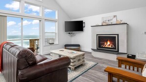 A modern living room with a fireplace, a television, and a view of the ocean.