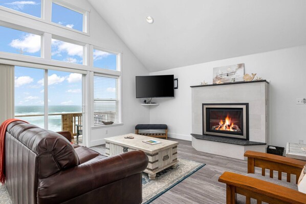 A modern living room with a fireplace, a television, and a view of the ocean.