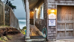 A wooden building with a porch overlooking the ocean, a sign for 'Whales Tale' and a contact number for 'itrip vacations'.