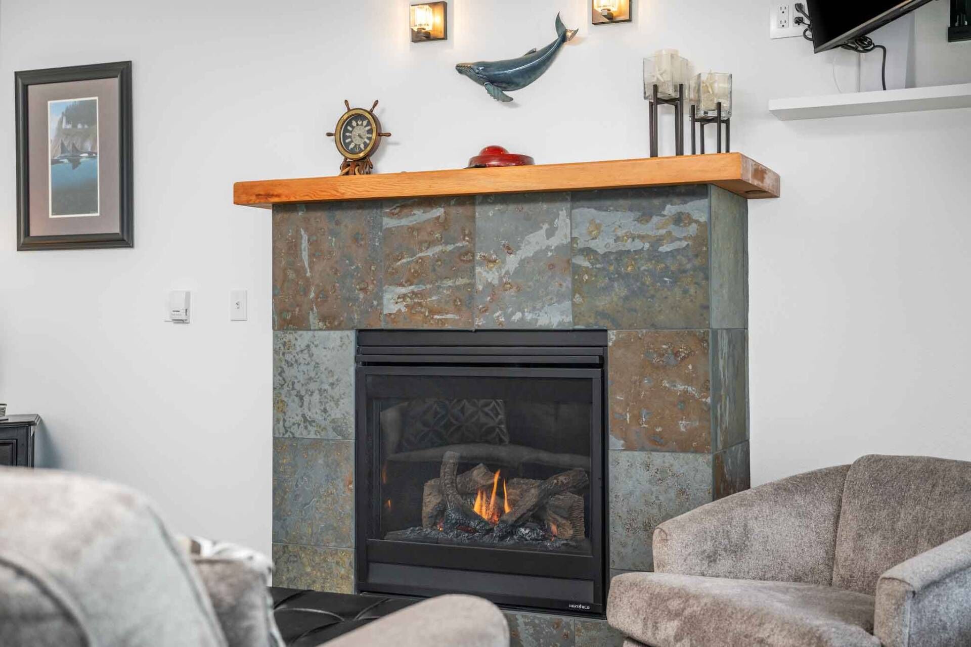Une cheminée avec un foyer en pierre rustique, une étagère ornée d’objets décoratifs et un tableau encadré accroché au mur.
