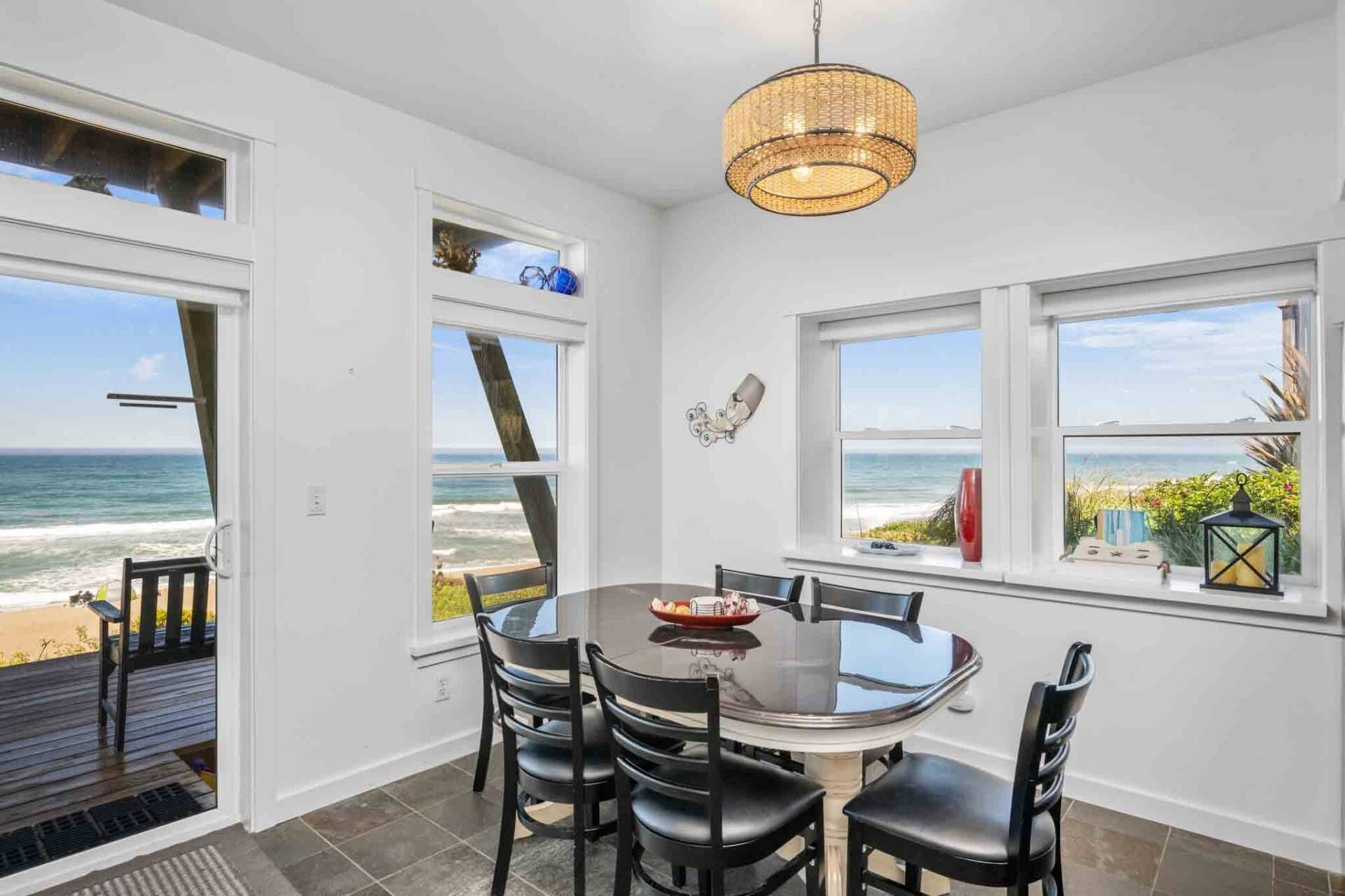 A dining area with a round table and chairs, large windows with ocean views, and a hanging light fixture.