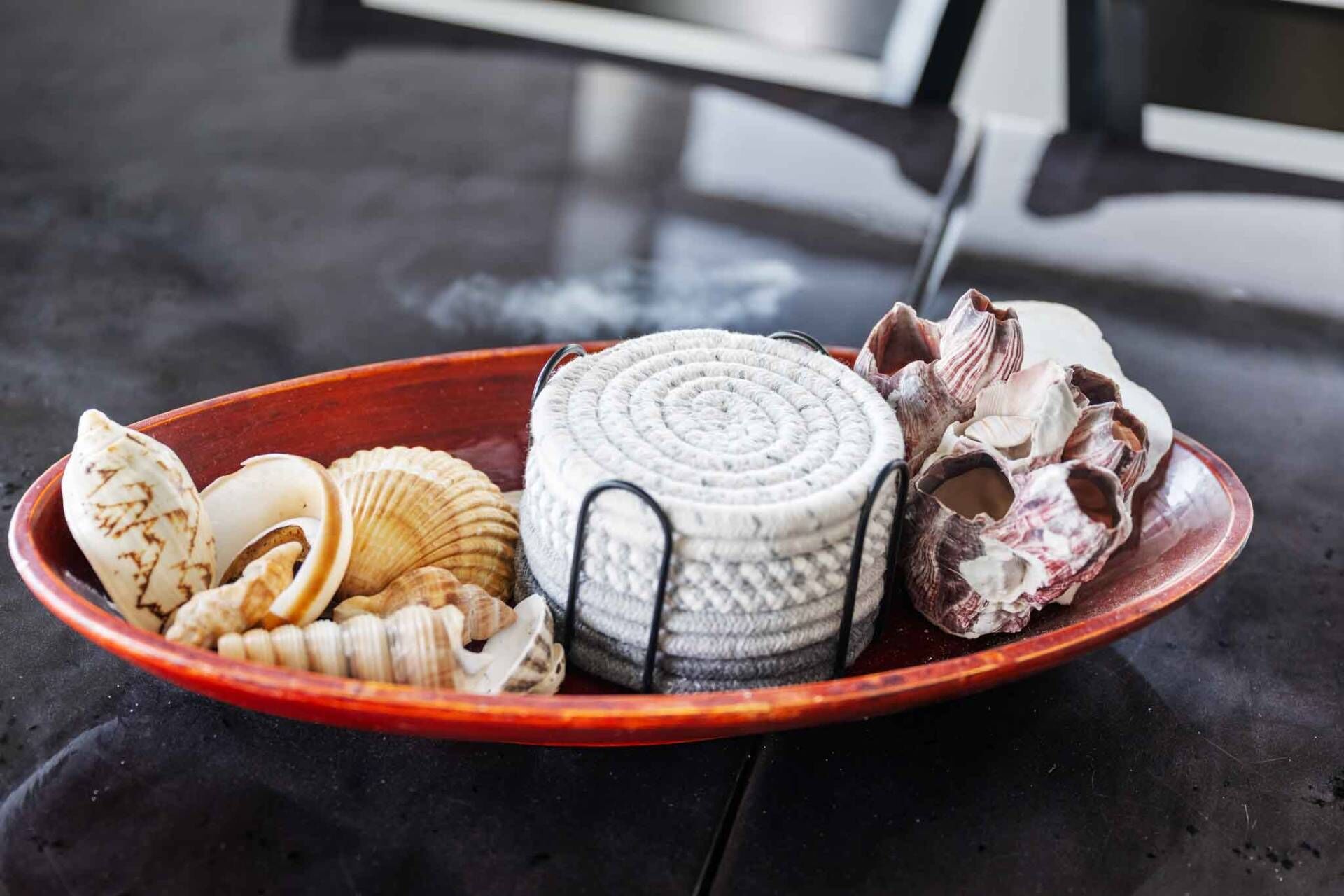 Ein roter Tablett mit verschiedenen Muscheln und einem gewebten Korb auf dunklem Untergrund.