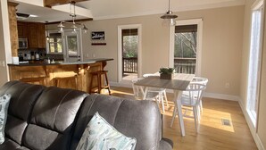 Amplia sala de estar con sofá de cuero, una mesa de comedor de madera con sillas, una zona de cocina con armarios de madera y ventanas grandes que permiten la entrada de luz natural.