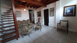 Uma sala de estar espaçosa com escada de madeira, área de jantar com móveis antigos e uma grande pintura na parede.