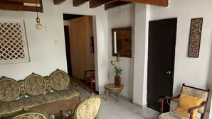 Uma área de refeições com mesa de madeira e quatro cadeiras, uma mesinha lateral com um vaso e uma porta com espelho e obras de arte.