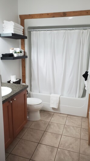 Ein Badezimmer mit Toilette, Waschbecken und Badewanne. Regale mit Handtüchern und Pflegeprodukten sind vorhanden.
