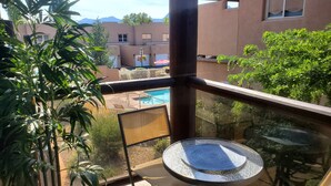 A balcony with a view of a swimming pool, potted plants, and a table with a glass top.
