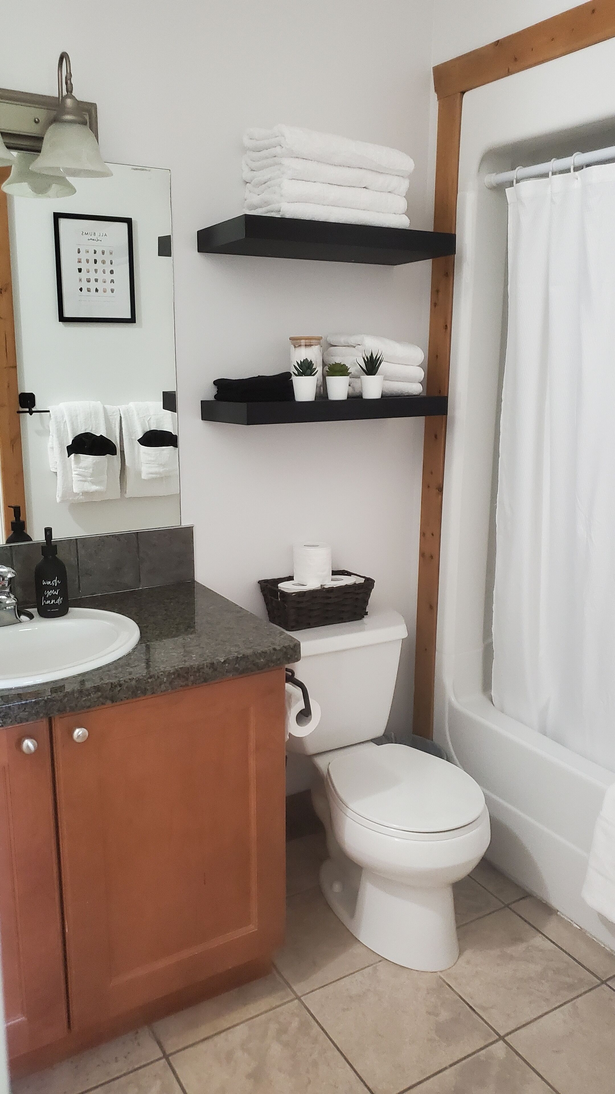 A bathroom with a sink, toilet, and shower curtain. There are shelves with towels and a framed picture on the wall.
