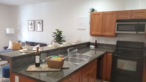 A modern kitchen with granite countertops, wooden cabinets, a stainless steel sink, and a black stove.