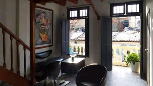 A room with a wooden staircase, a black chair, a small table, and a painting on the wall. - 2G2-2 Apartamento en la Ciudad Antigua (Cartagena)