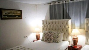 A hotel room with a large bed, two bedside tables with lamps, a window with curtains, and a painting on the wall. - 2G2-2 Apartamento en la Ciudad Antigua (Cartagena)