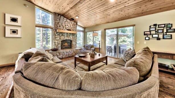 Una sala de estar acogedora con chimenea de piedra, ventanas amplias y techo de madera.