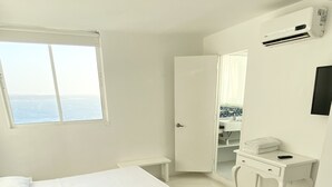 Une chambre d’hôtel moderne, équipée d’un lit, d’un bureau et d’une salle de bain, visible à travers une porte ouverte.