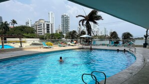 Une piscine entourée de bâtiments de grande hauteur, avec des chaises longues et des palmiers.